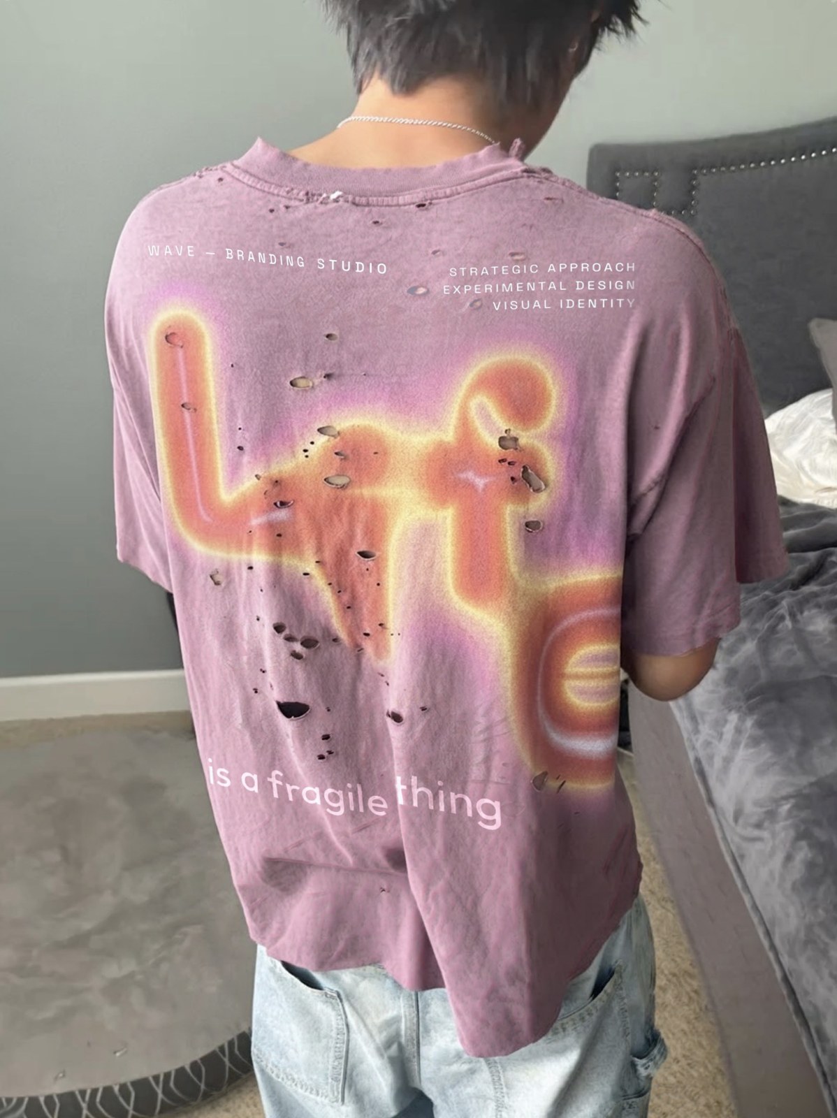 Back of a washed mauve distressed T-shirt: the word Life in large glowing living letters, the line is a fragile thing, the studio caption and notes